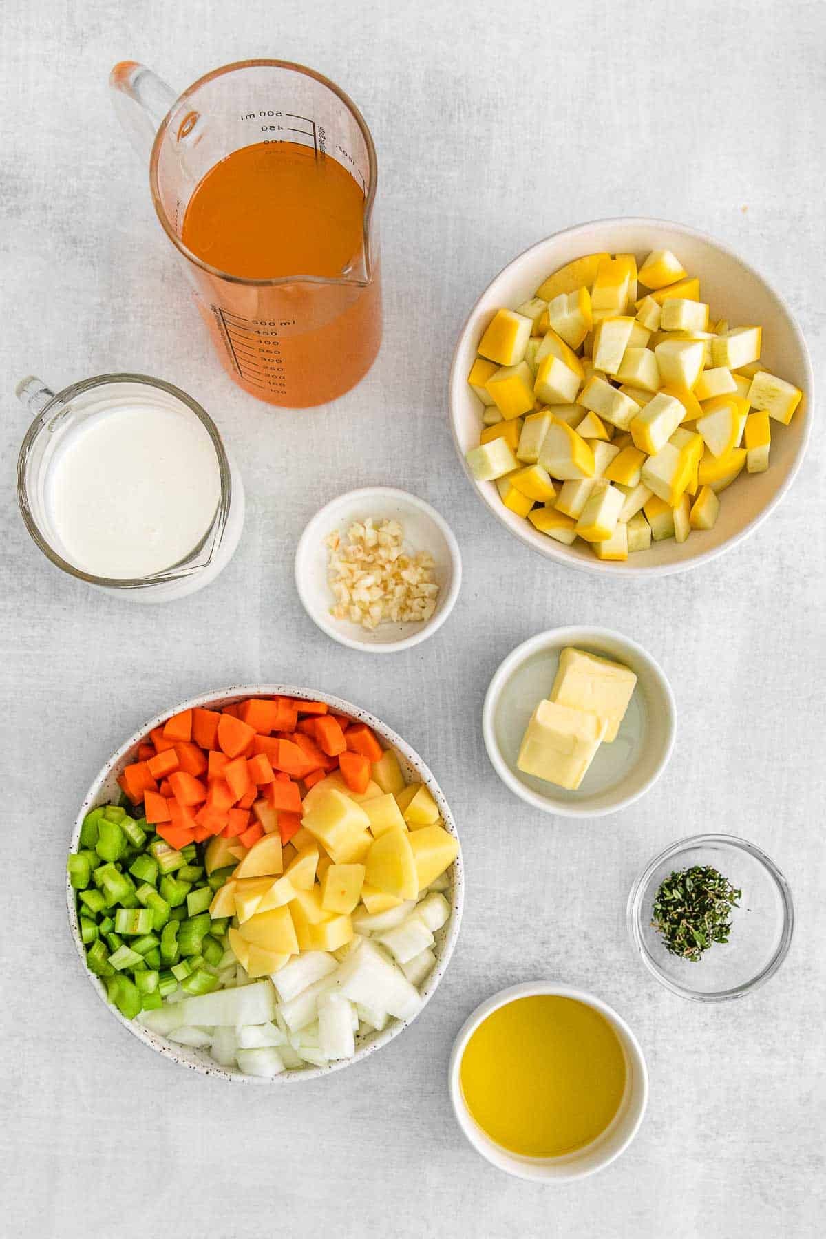 Several bowls of ingredients for Yellow Squash Soup - Olive oil, onion, carrots, celery, Yukon gold potato, yellow squash, garlic, thyme, vegetable broth, heavy cream and butter.