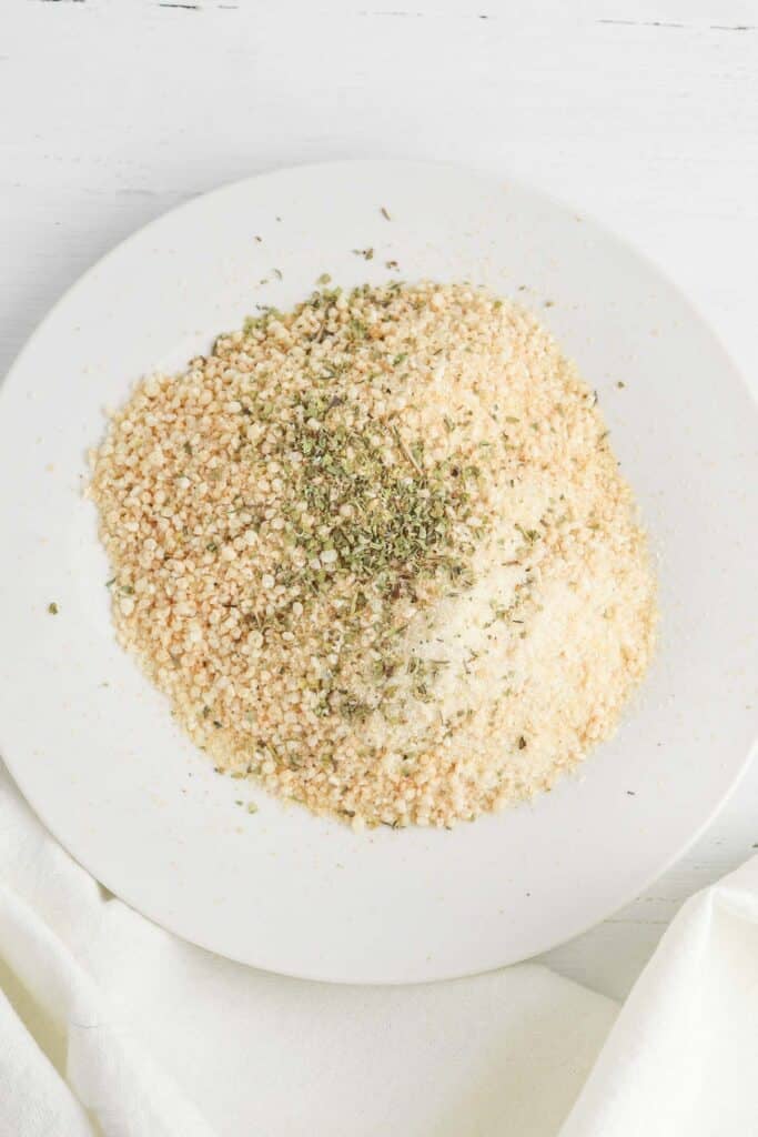 The breadcrumbs, garlic powder, and Italians seasoning mixed together on white plate.