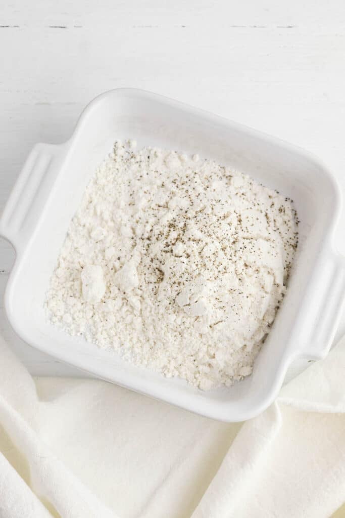 Flour, salt, and pepper mixed together in white bowl.