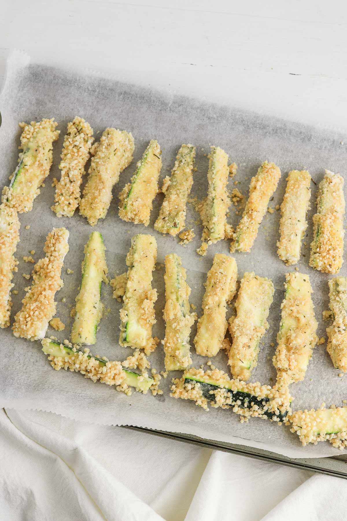 Zucchini strips coated in breading mixture laid out on baking sheet.