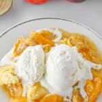 Close up of peach dump cake with a scoop of vanilla ice cream on a white plate.