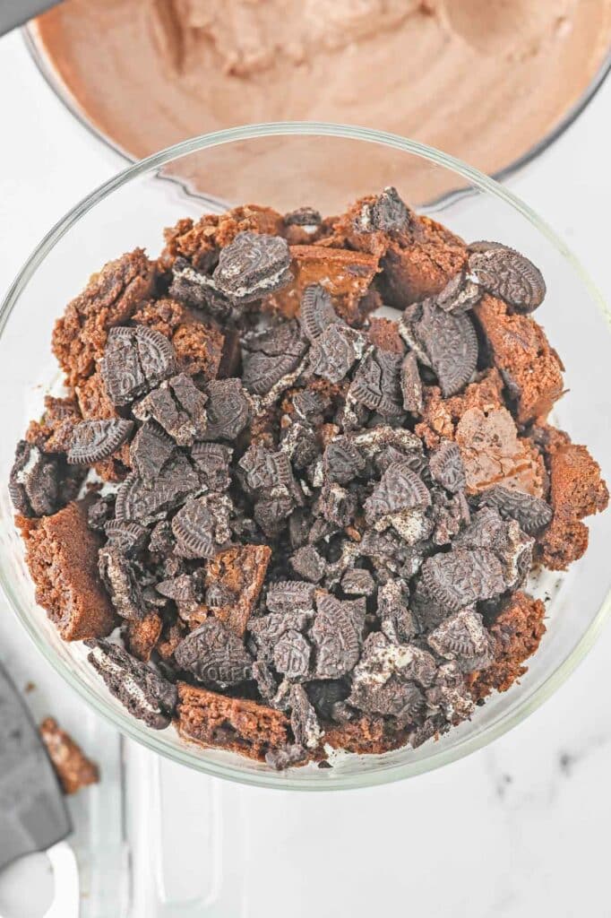 Crumbled oreos added to large glass mixing bowl over brownies.