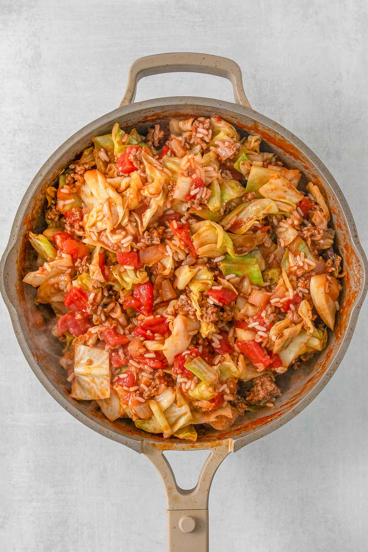 Sauteed cabbage and diced tomatoes in a skillet on a grey background.