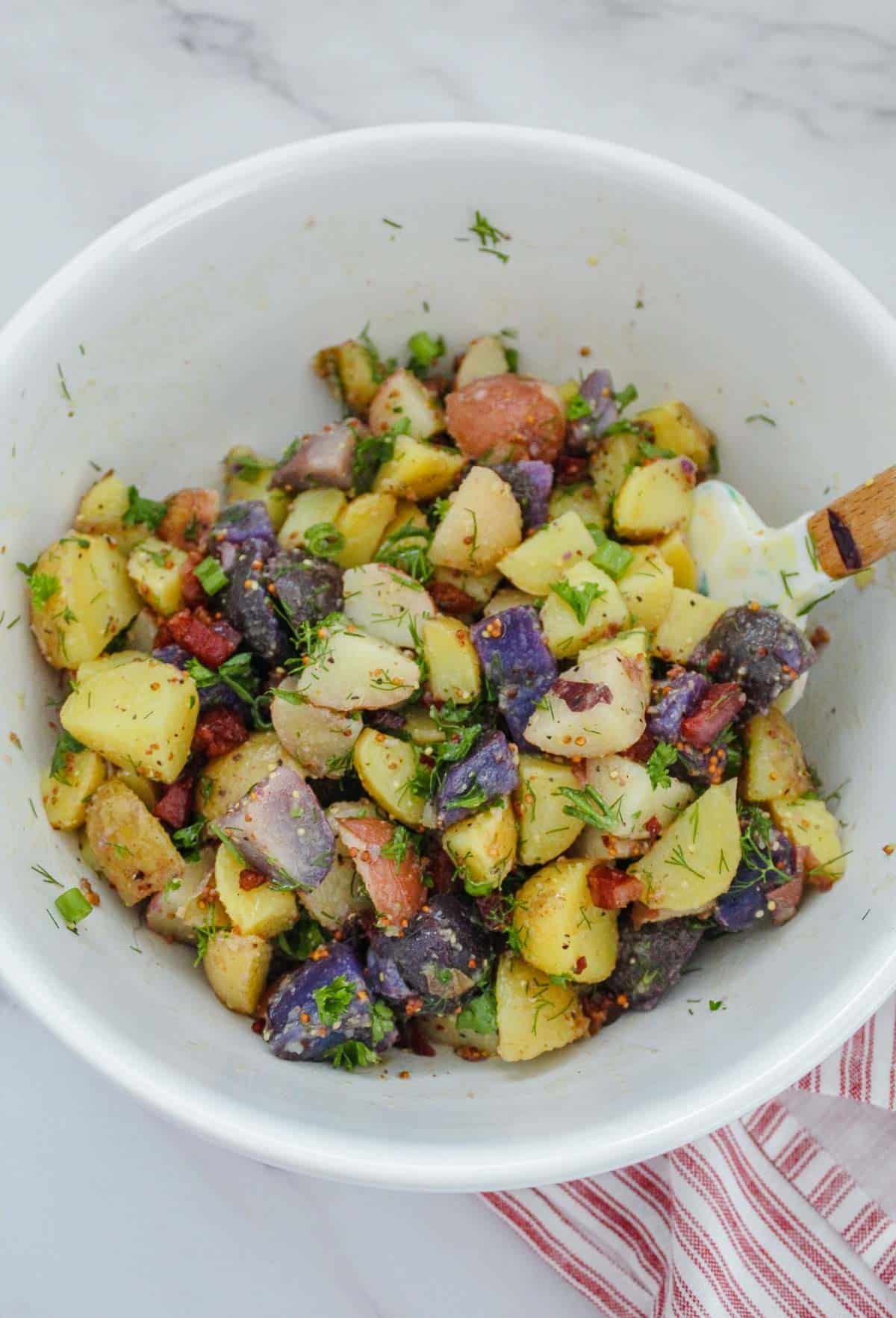 A white bowl filled with cubed tri-colored potatoes and herbs.