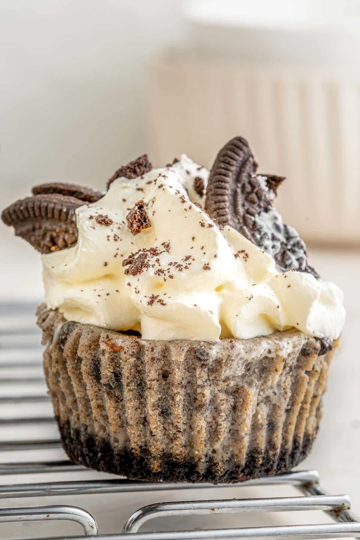 Oreo cupcakes topped with whipped cream and oreos on a cooling rack.