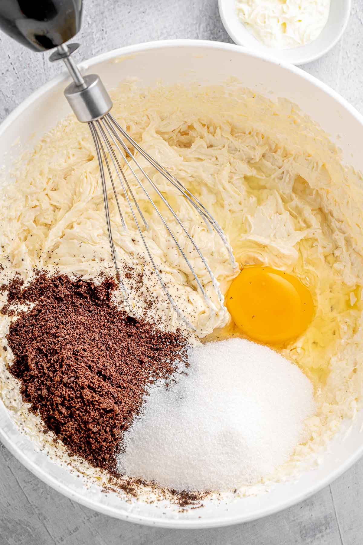 Whisking ingredients for oreo cheesecake cupcakes in a white bowl.