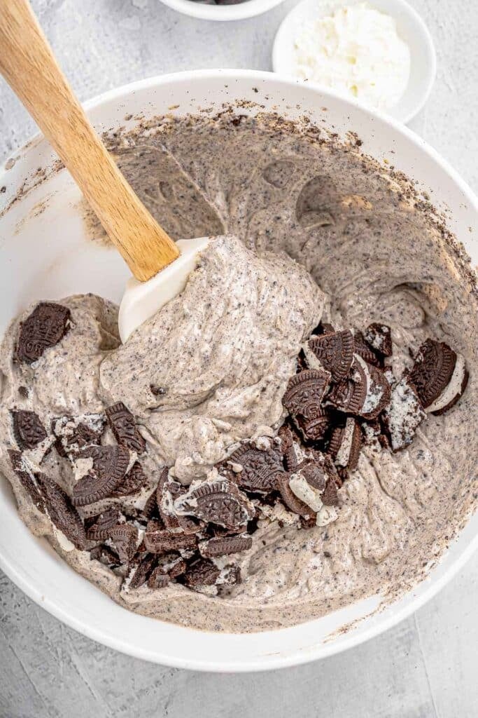 Oreo cookie batter in a bowl with a wooden spoon.