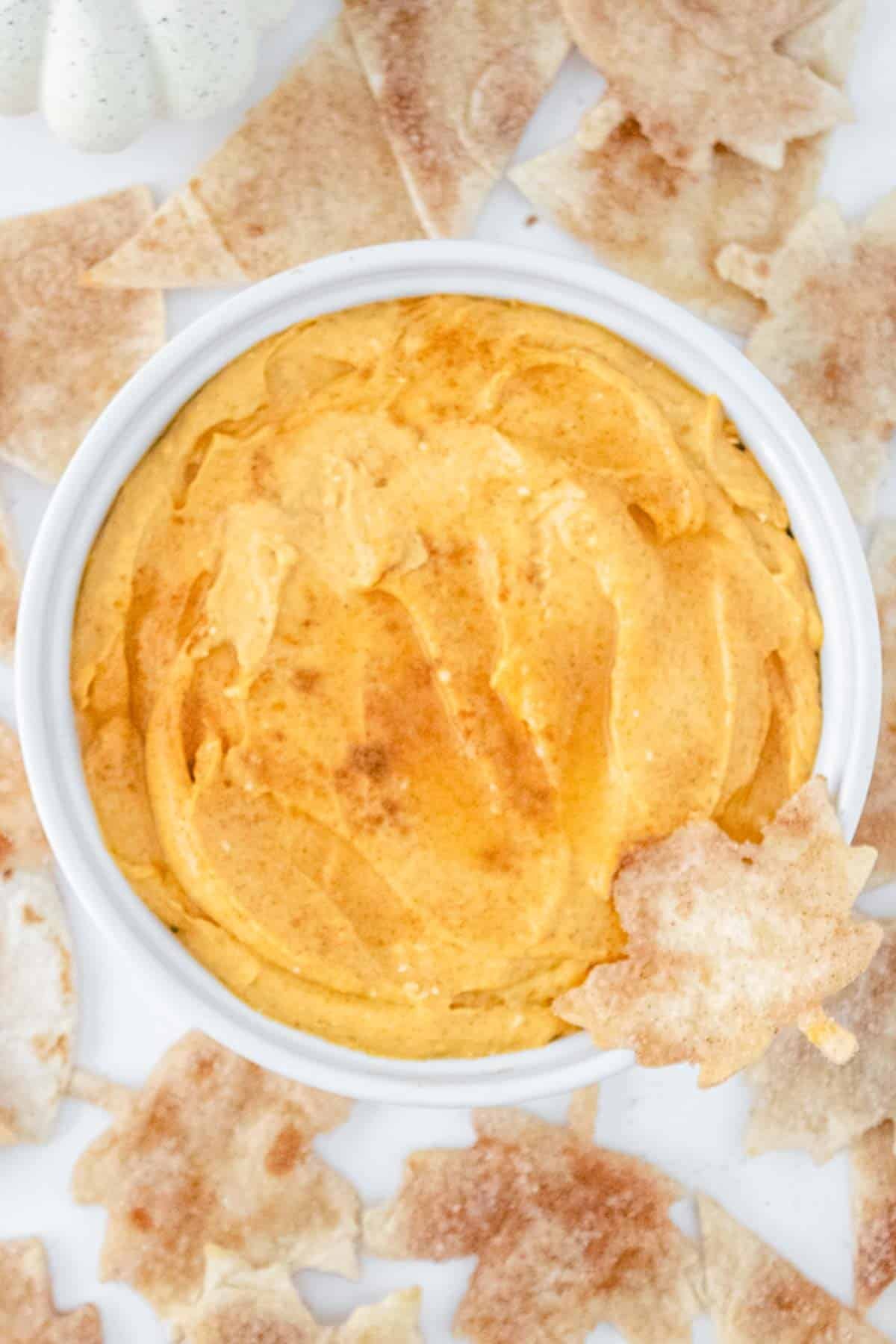 A bowl of pumpkin cheesecake dip in a white bowl surrounded by tortilla chips.