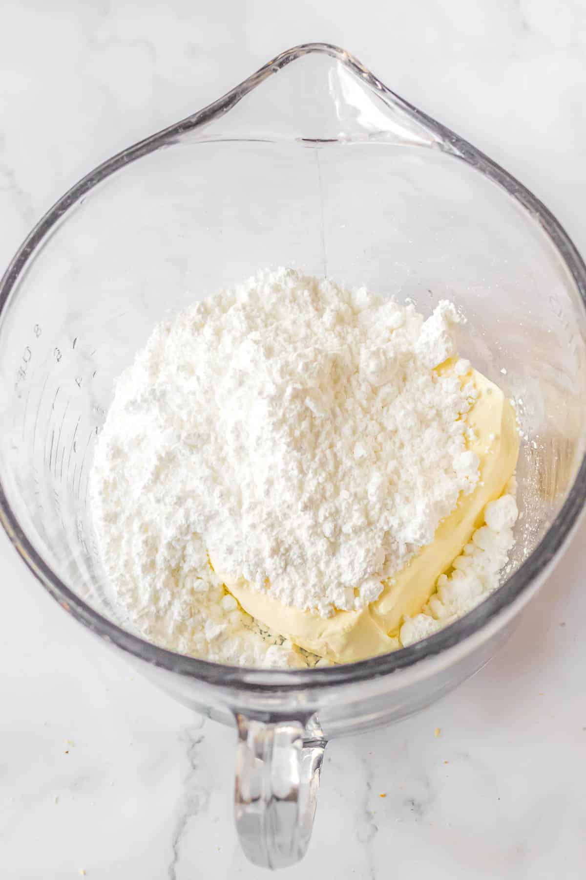 A glass bowl with cream cheese, butter and powdered sugar in it.