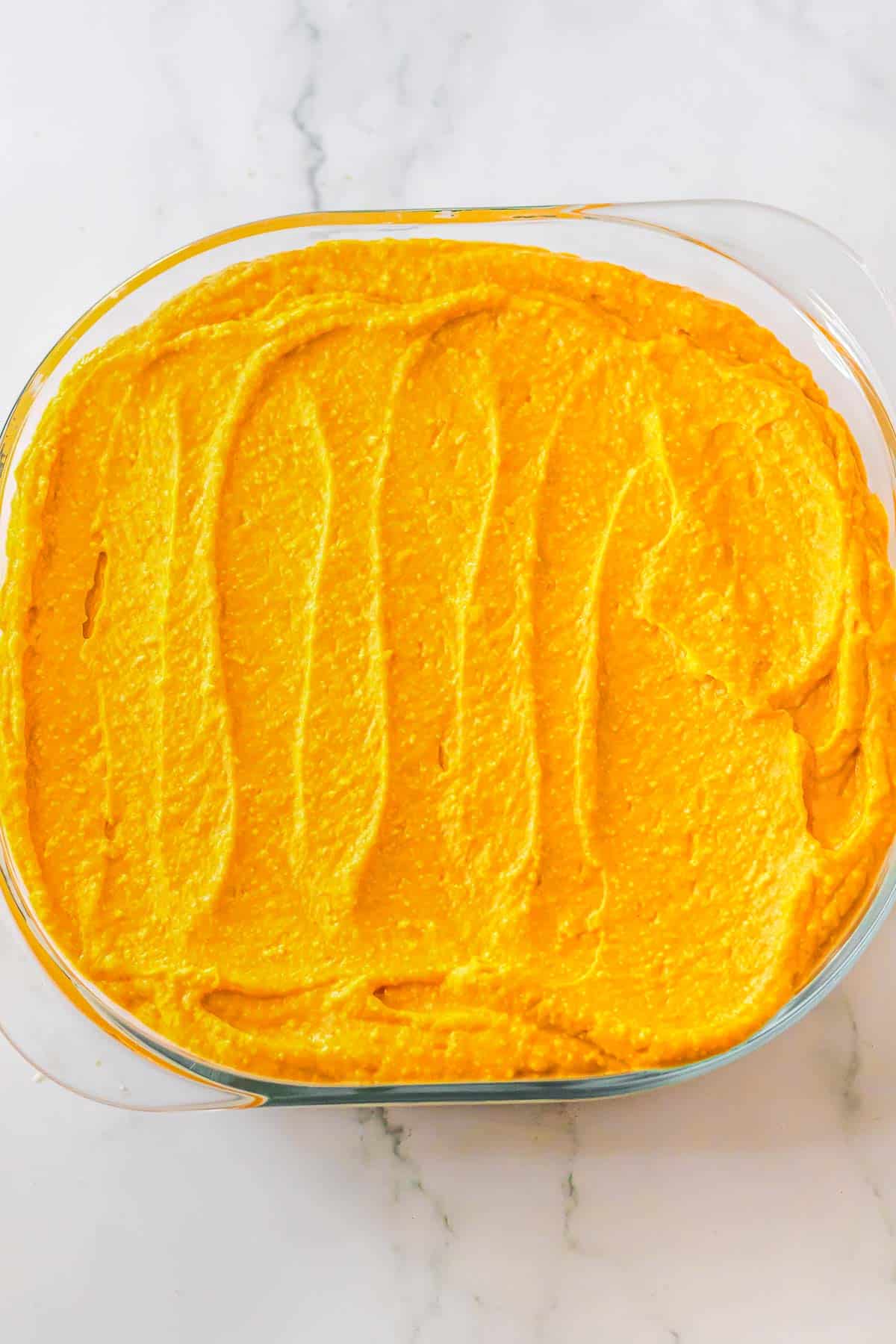 A glass baking dish with pumpkin mix over cream cheese mixture.