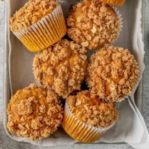 Multiple pumpkin oat muffins on a baking sheet with crumb topping.