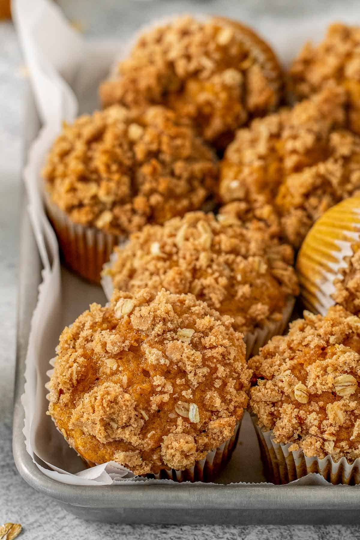 Multiple pumpkin oat muffins on a baking sheet with crumb topping.