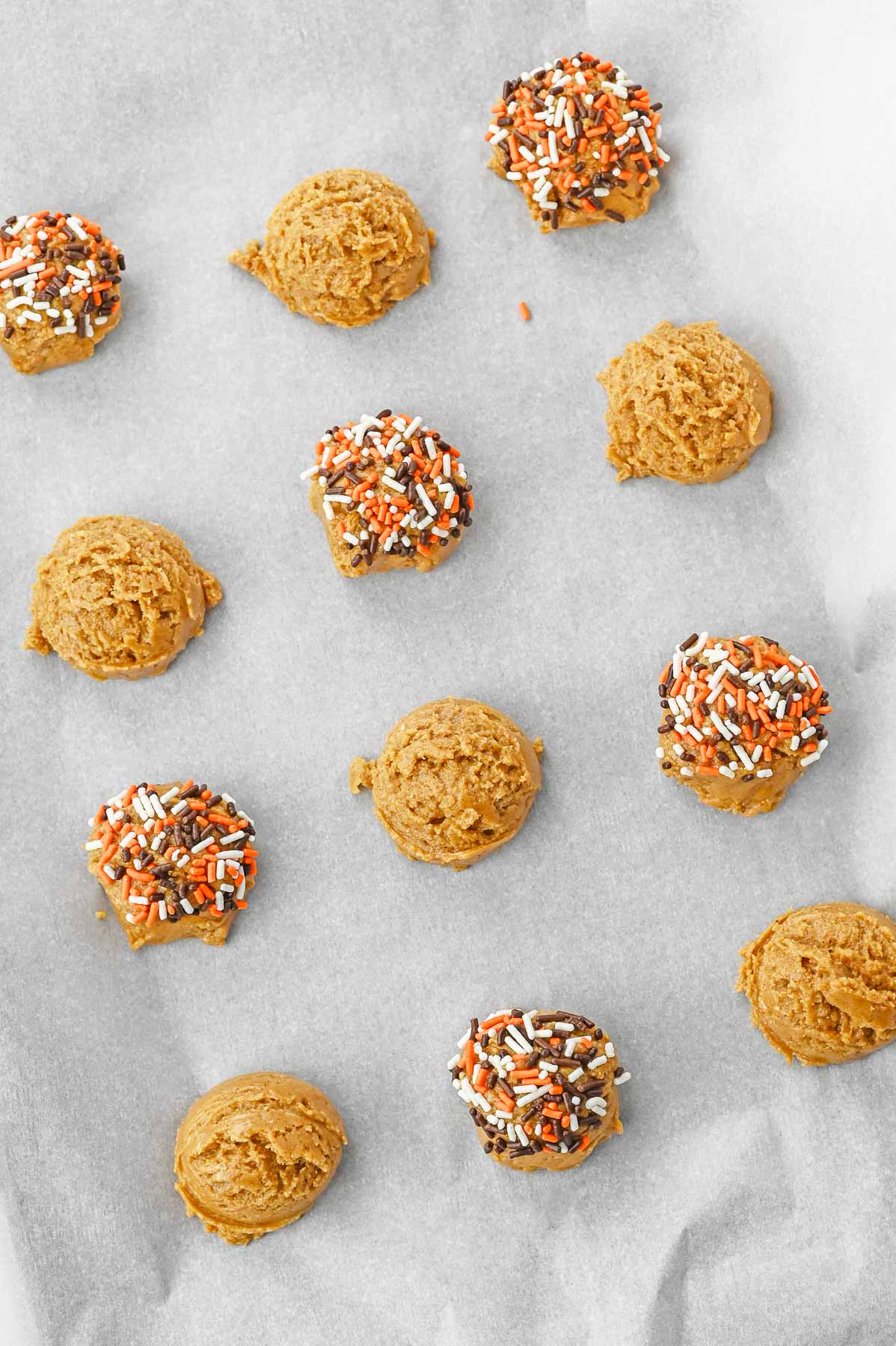Pumpkin spice cookie dough balls with sprinkles on a baking sheet.