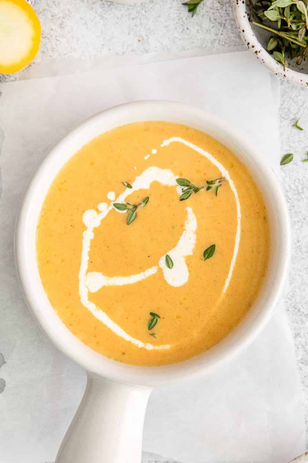 Yellow Squash Soup in small white bowl with handle topped with fresh herbs.