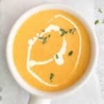 Yellow Squash Soup in small white bowl with handle topped with fresh herbs.