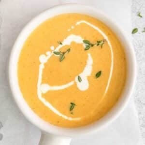 Yellow Squash Soup in small white bowl with handle topped with fresh herbs.