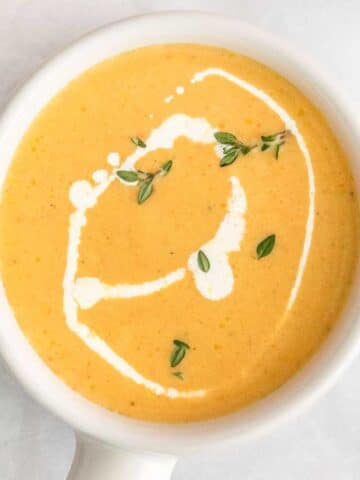 Yellow Squash Soup in small white bowl with handle topped with fresh herbs.