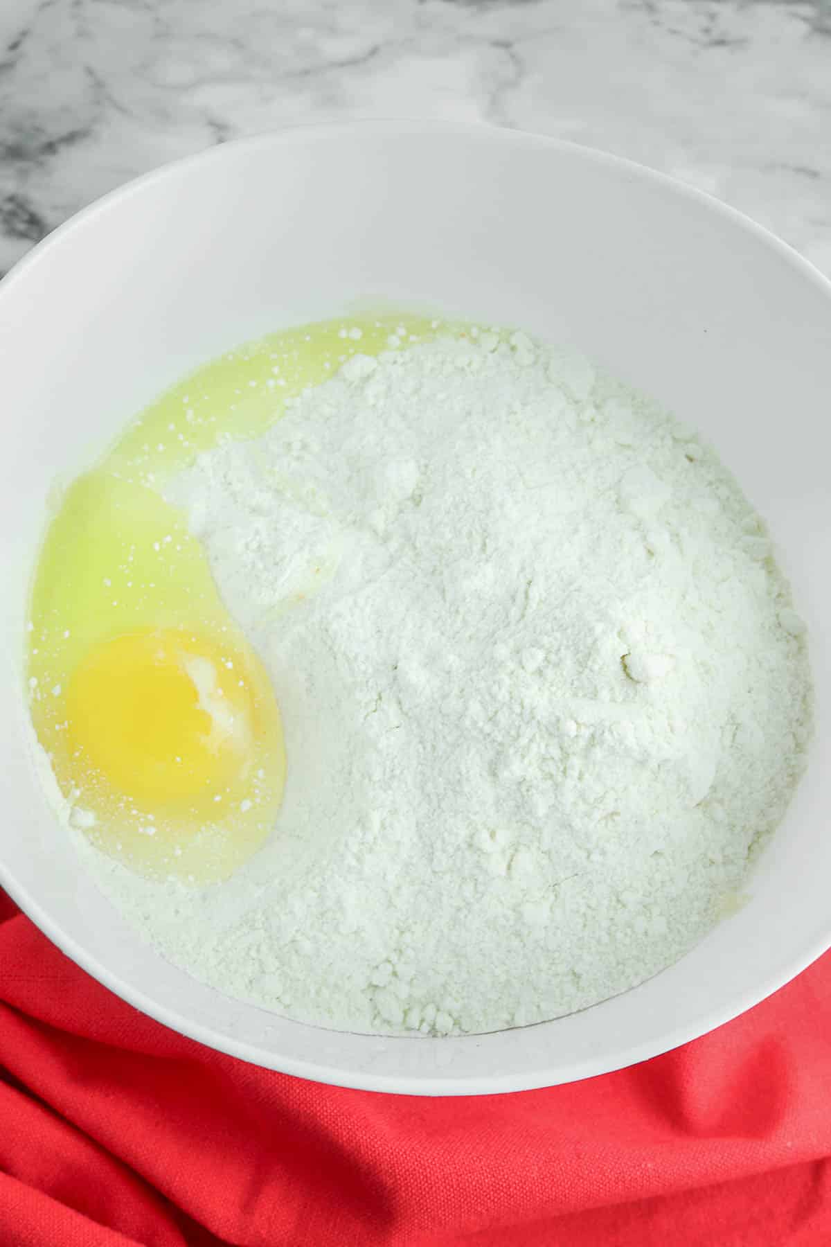 A white mixing bowl with an egg and yellow cake mix in it.