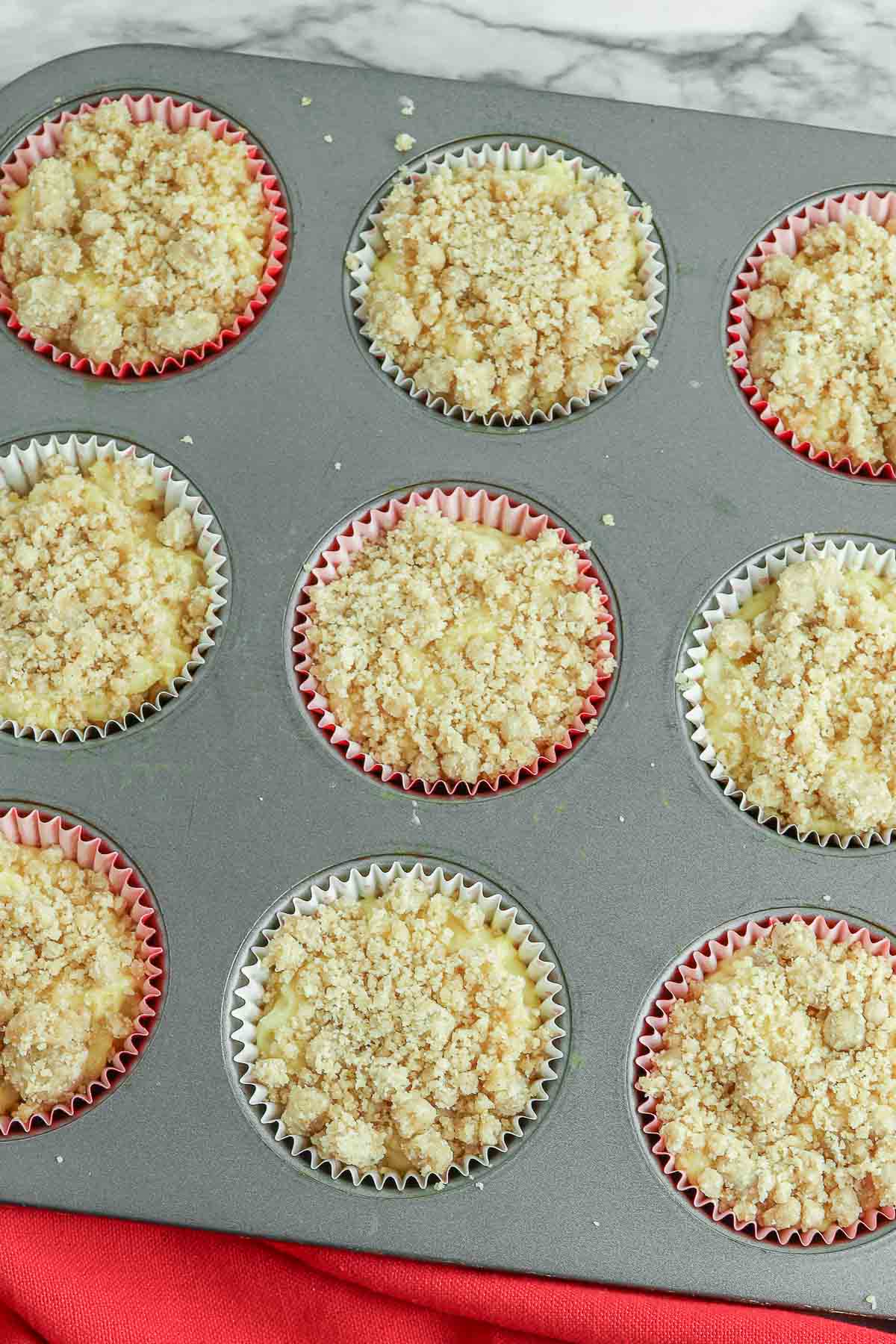 Cinnamon crumble topping spread over muffins in a muffin tin.