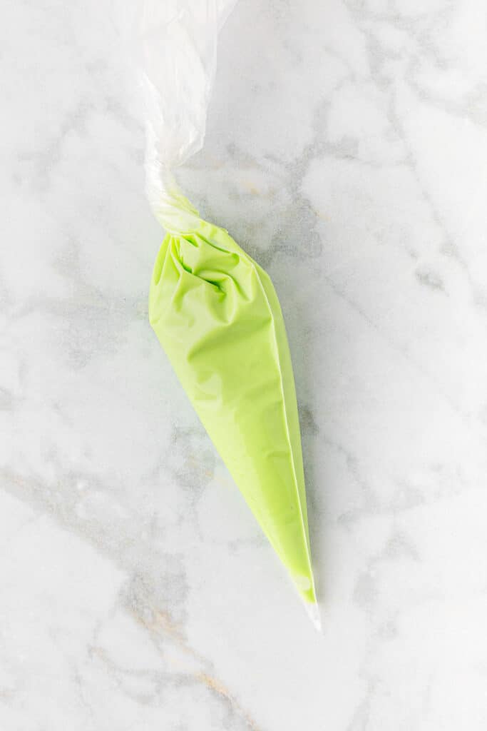 A plastic piping bag with green icing on a marble table.