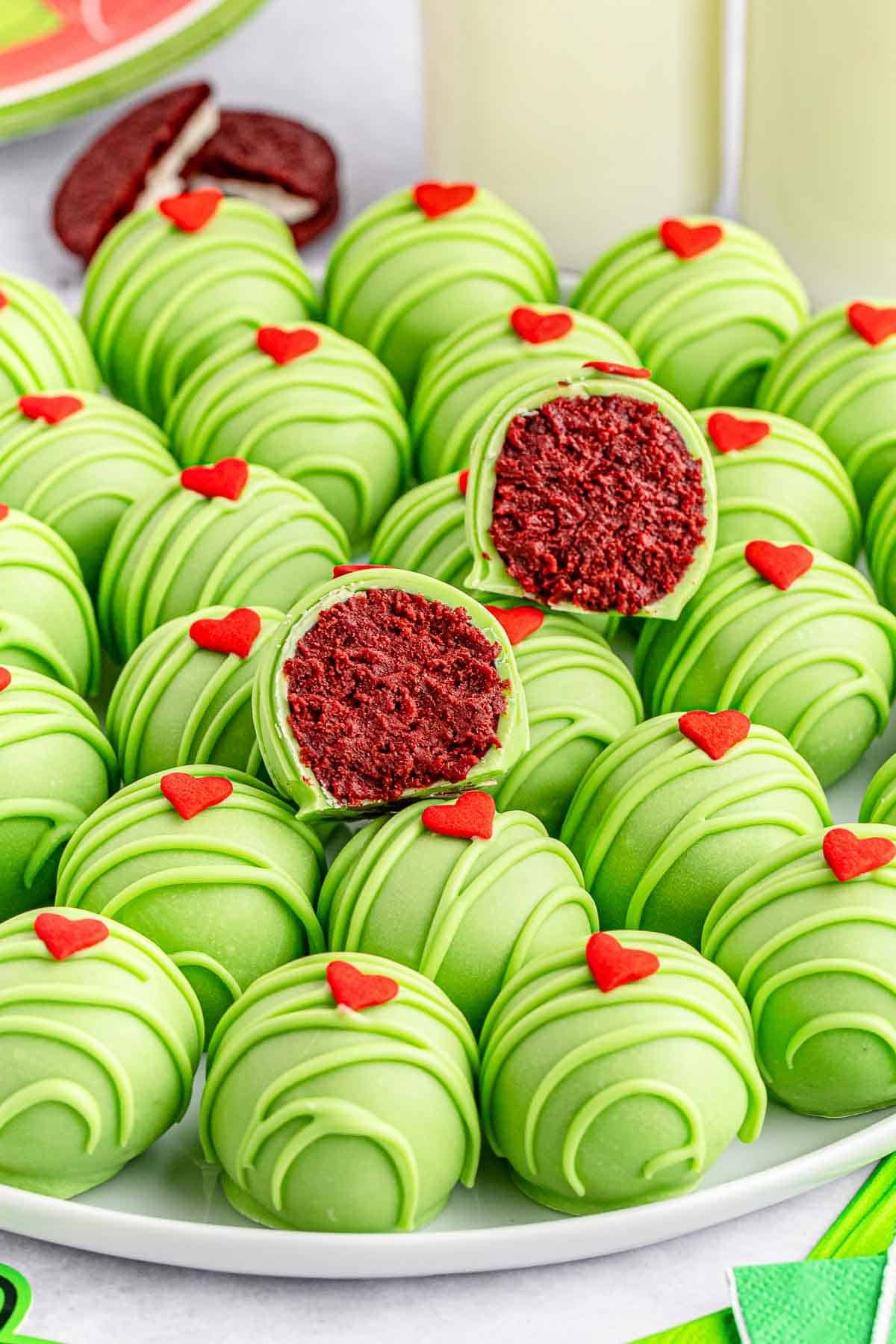 A white plate full of green grinch balls topped with a red candy heart with 2 sliced in half showing the red cookie center.