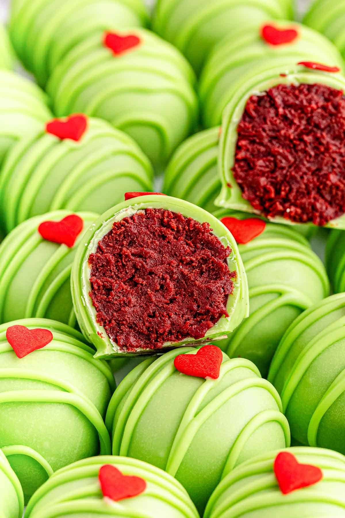 A bunch of green grinch oreo balls with red candy hearts on them and 2 cut in half showing a red velvet center..
