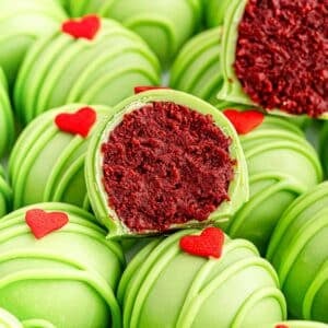 A bunch of green grinch oreo balls with red candy hearts on them and 2 cut in half showing a red velvet center..