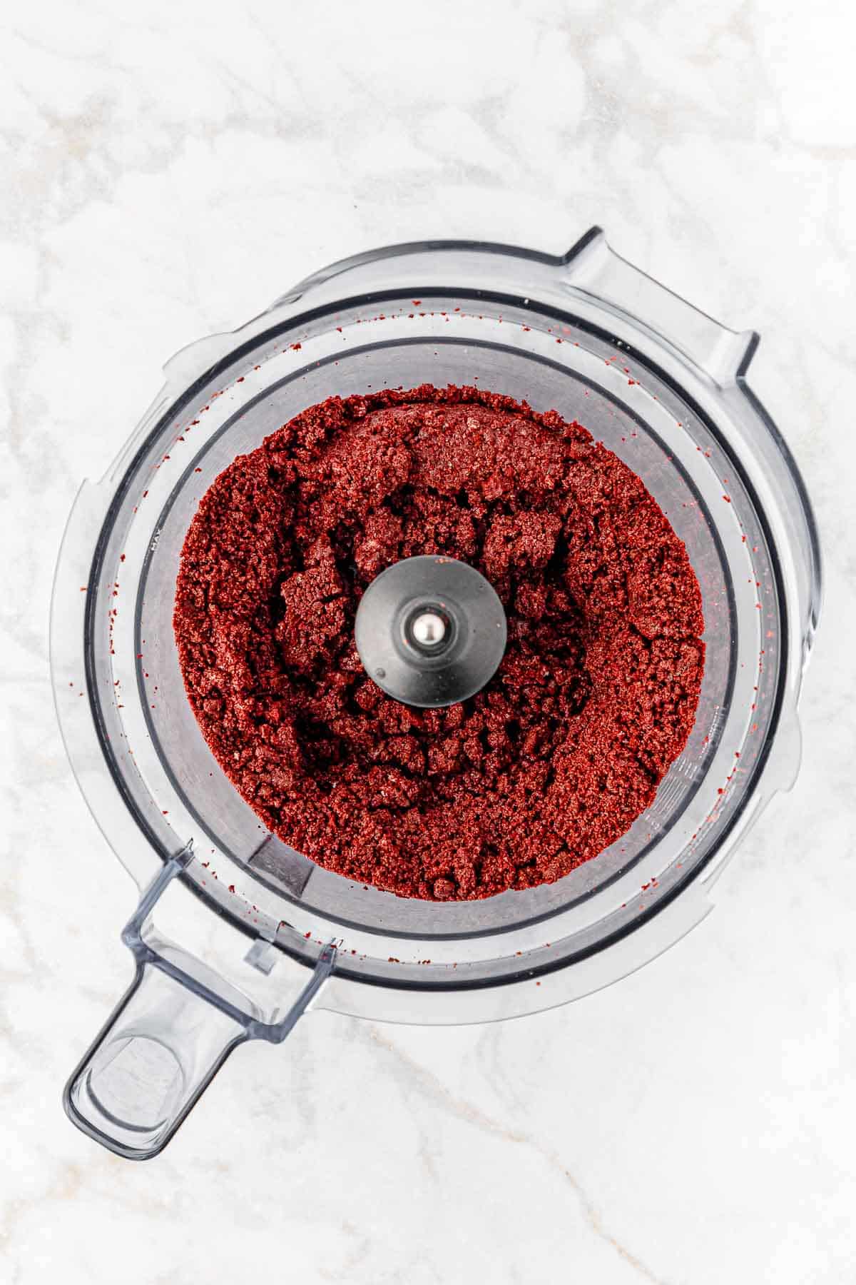 crushed red velvet oreos in a food processor on a marble countertop.