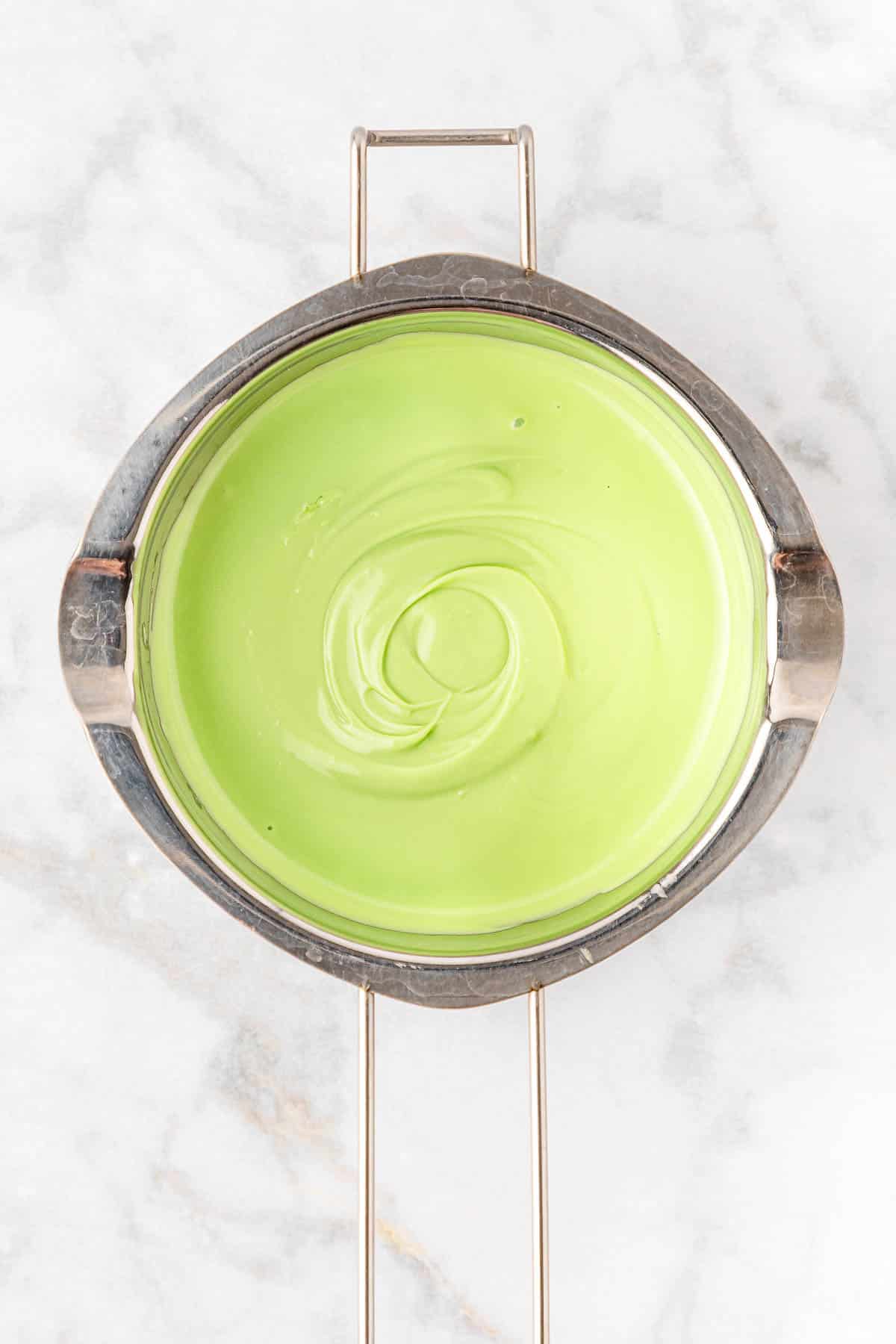 A stainless steel pot of green icing sitting on top of a marble table.