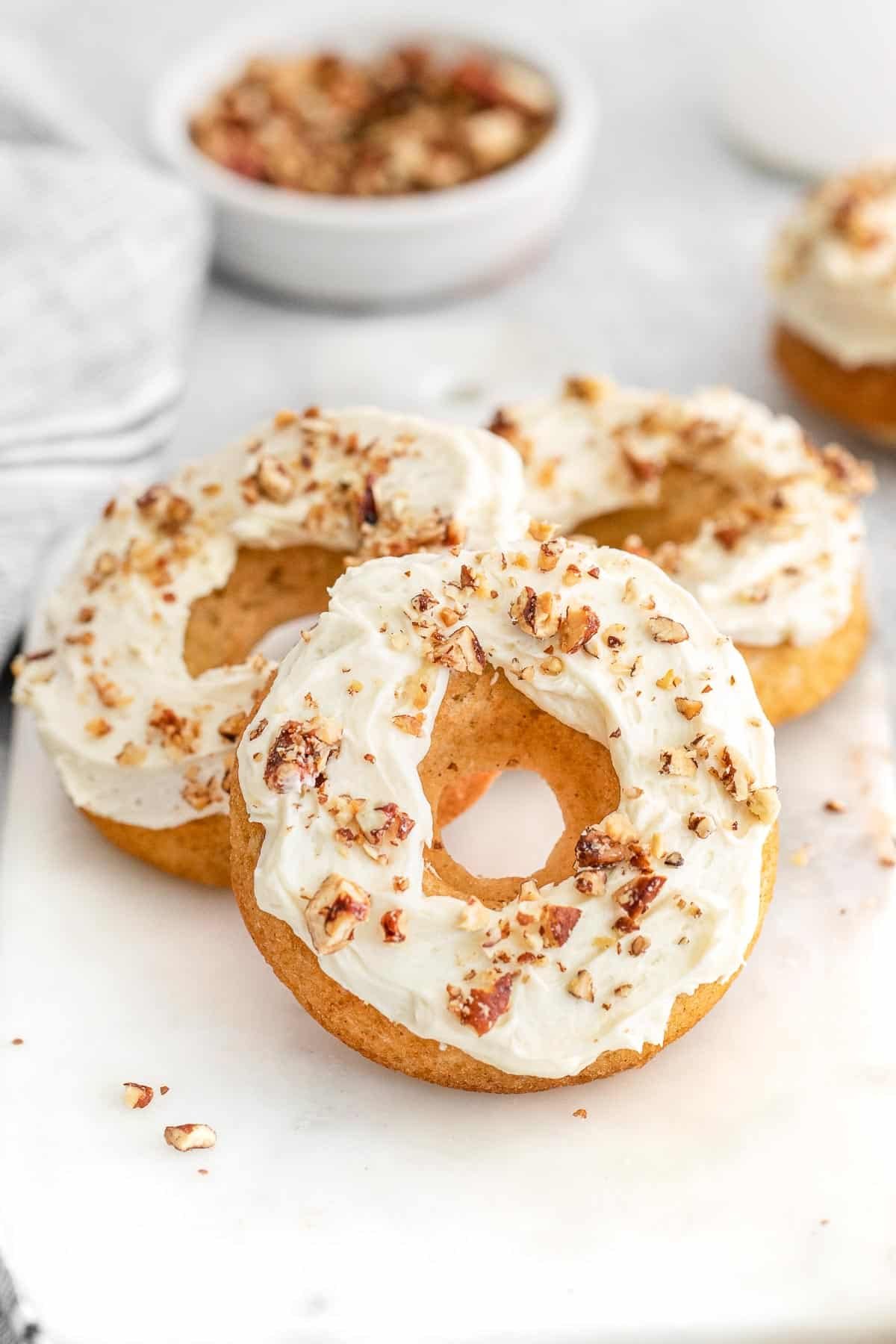 Several maple donuts topped with pecans on a white tray.