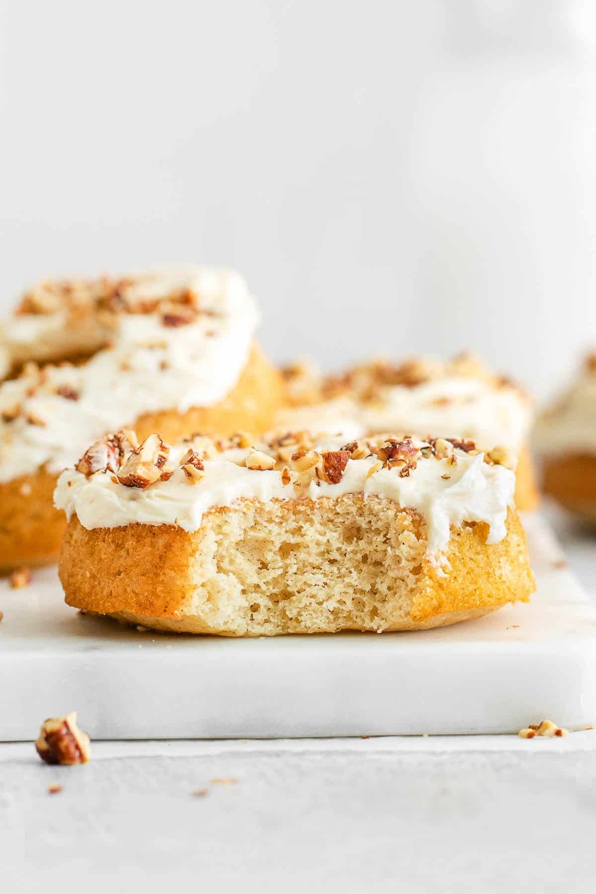 Maple donuts with a bite taken out topped with frosting and pecans on a white cutting board.
