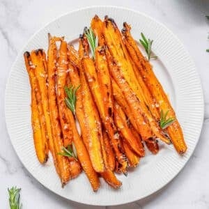 Maple Glazed Carrots on a white plate with rosemary.