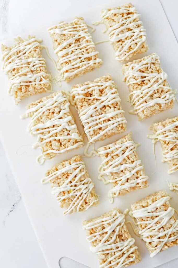 Rice krispie treats with white icing on a white cutting board.