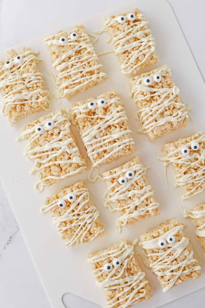 twelve mummy rice krispy treats on a white plate.