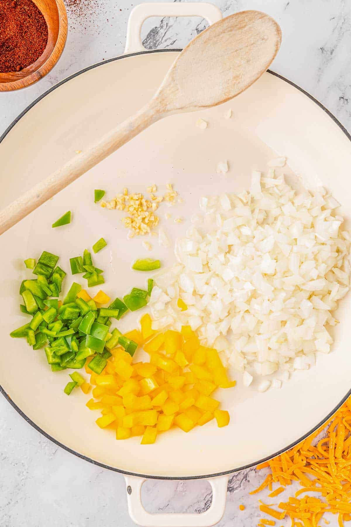 Chopped onion, yellow bell pepper and green bell pepper in a white pot.