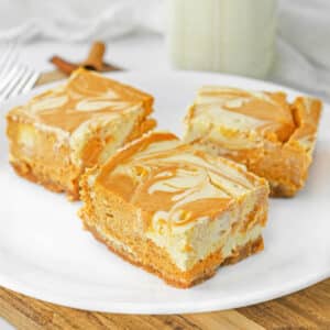 Three pumpkin pie cheesecake bars on a white plate.