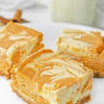 Three pumpkin pie cheesecake bars on a white plate.