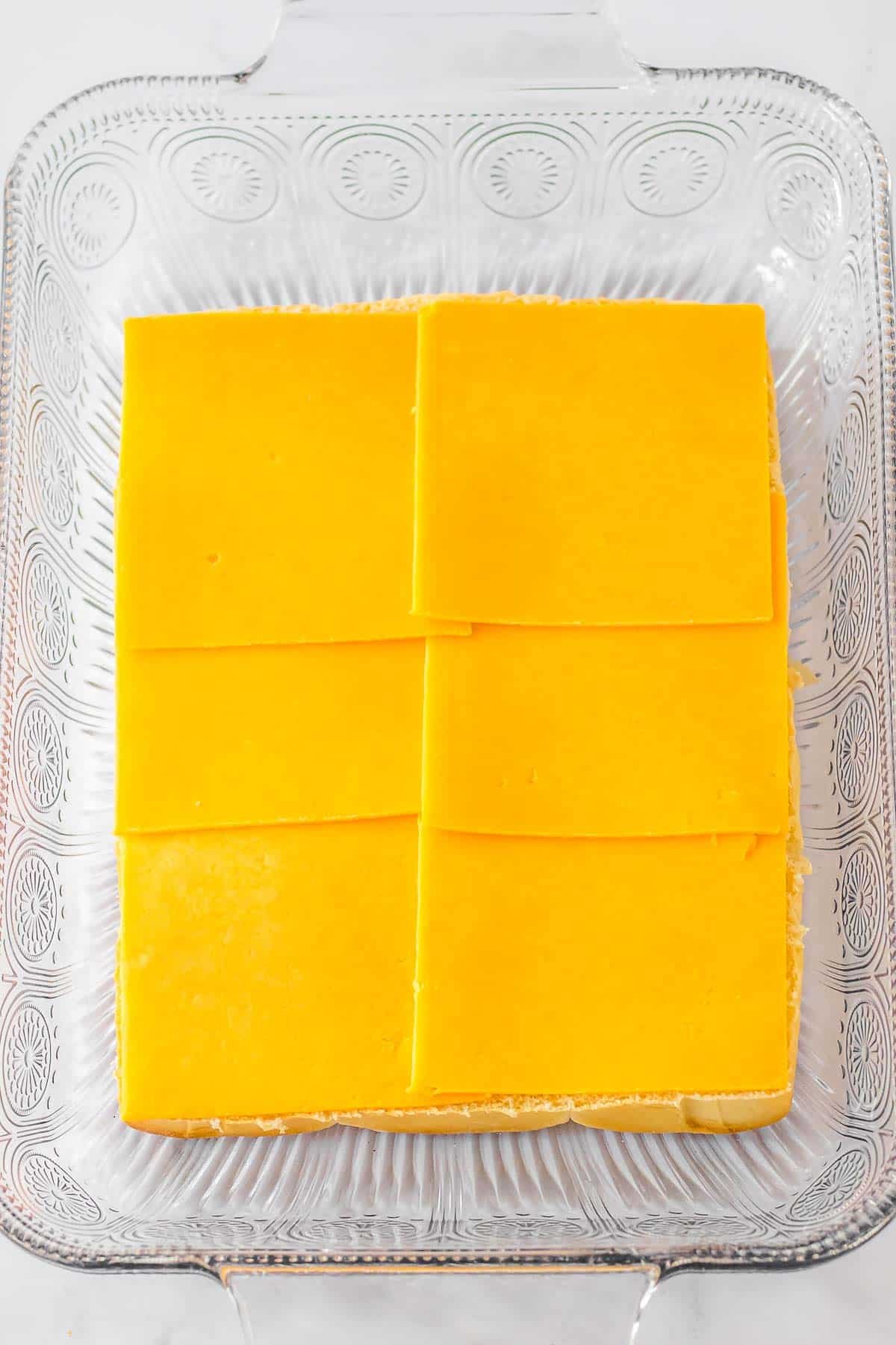 Cheese slices lining hawaiian rolls in a baking dish.