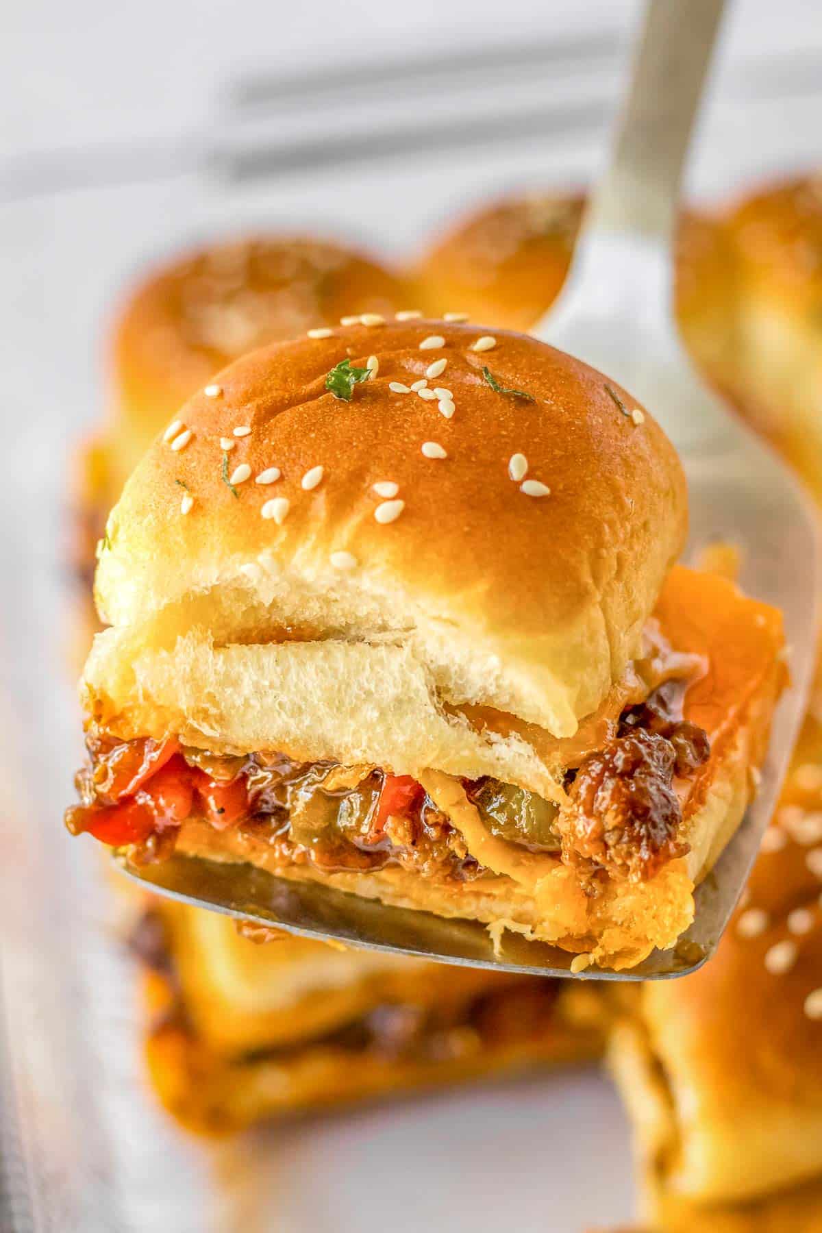 A spatula being used to pick up a Sloppy Joe Slider off of white plate.