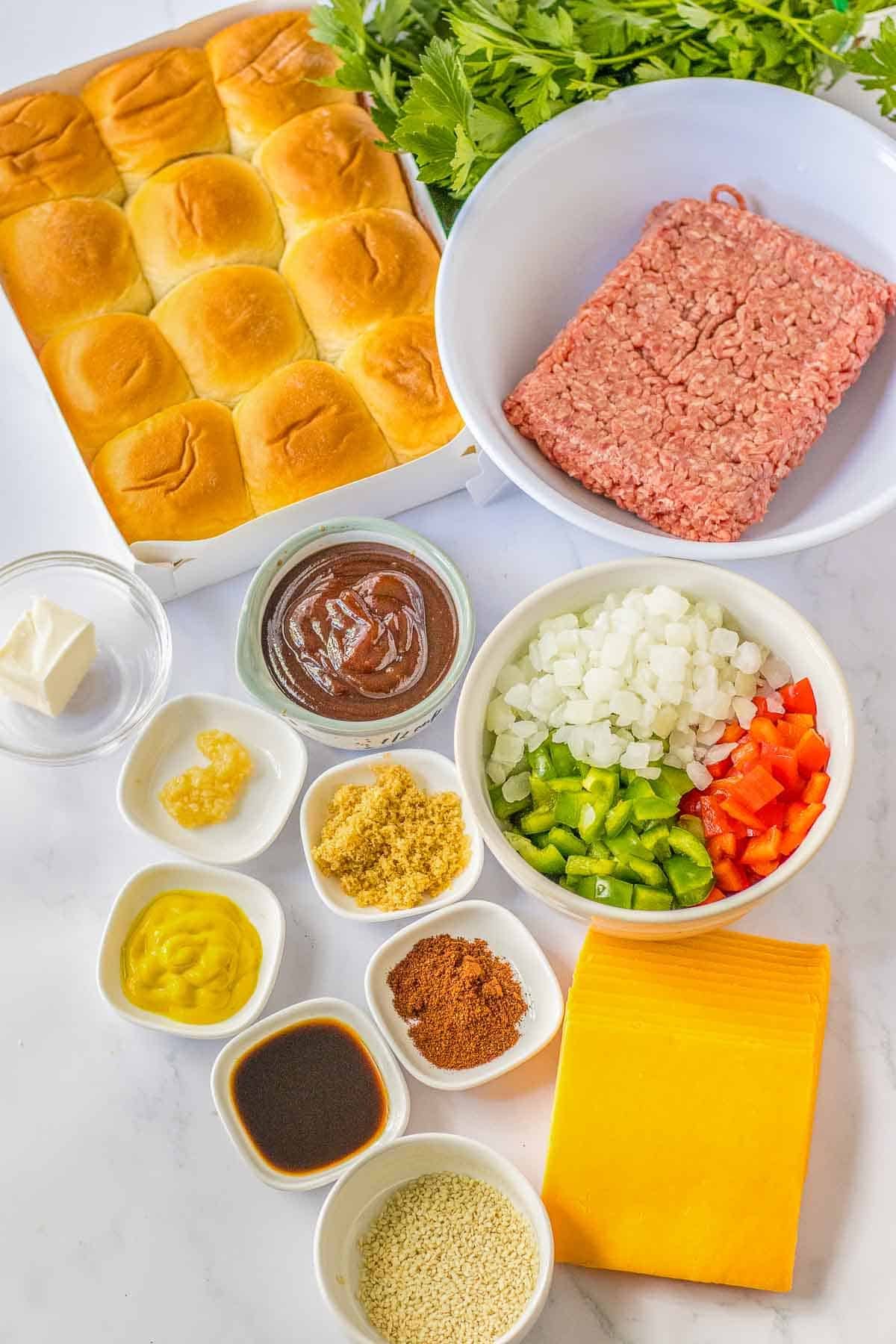 Ingredients for Sloppy Joe Sliders - Ground beef, red bell pepper, green bell pepper, onion, garlic, bbq sauce, chili powder, brown sugar, mustard, worcestershire sauce, cheddar cheese, Hawaiian rolls, butter, sesame seeds and parsley.