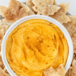 A bowl of pumpkin dip in a white bowl surrounded by cinnamon tortilla chips.