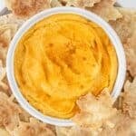 A bowl of pumpkin dip in a white bowl surrounded by cinnamon tortilla chips.