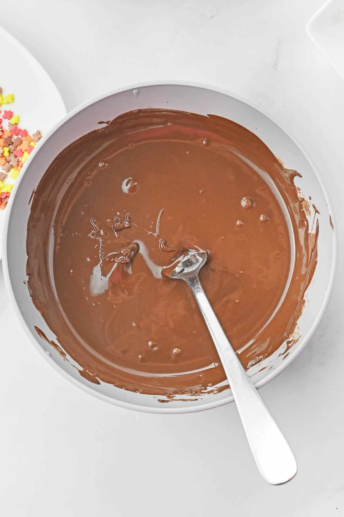 A bowl of melted chocolate with a spoon in it.