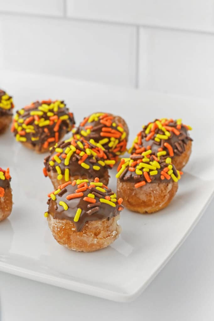 Donut holes dipped in chocolate with orange and yellow sprinkles on a white plate.