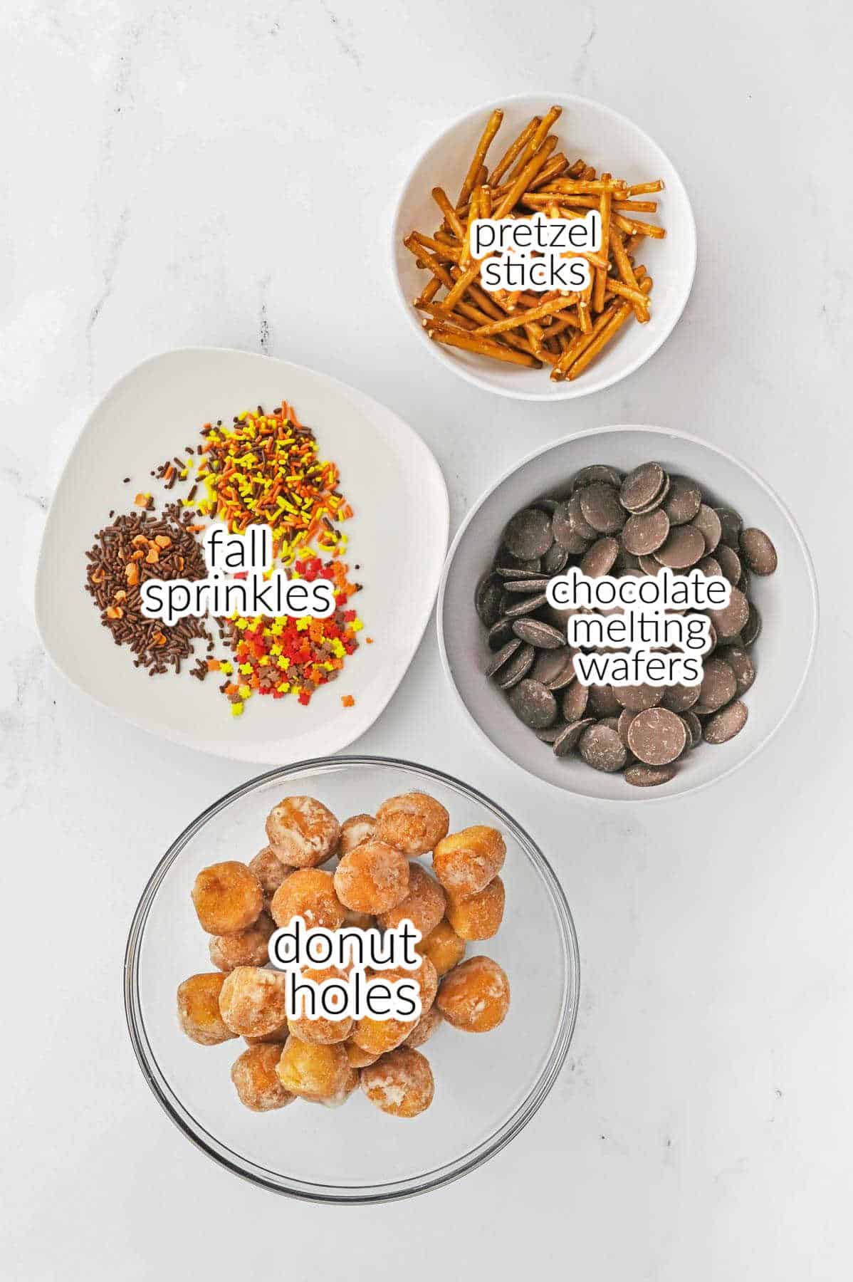 Donut holes, chocolate wafers, pretzel sticks and fall sprinkles in a white bowls.