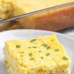A slice of corn casserole on a white plate with a fork.
