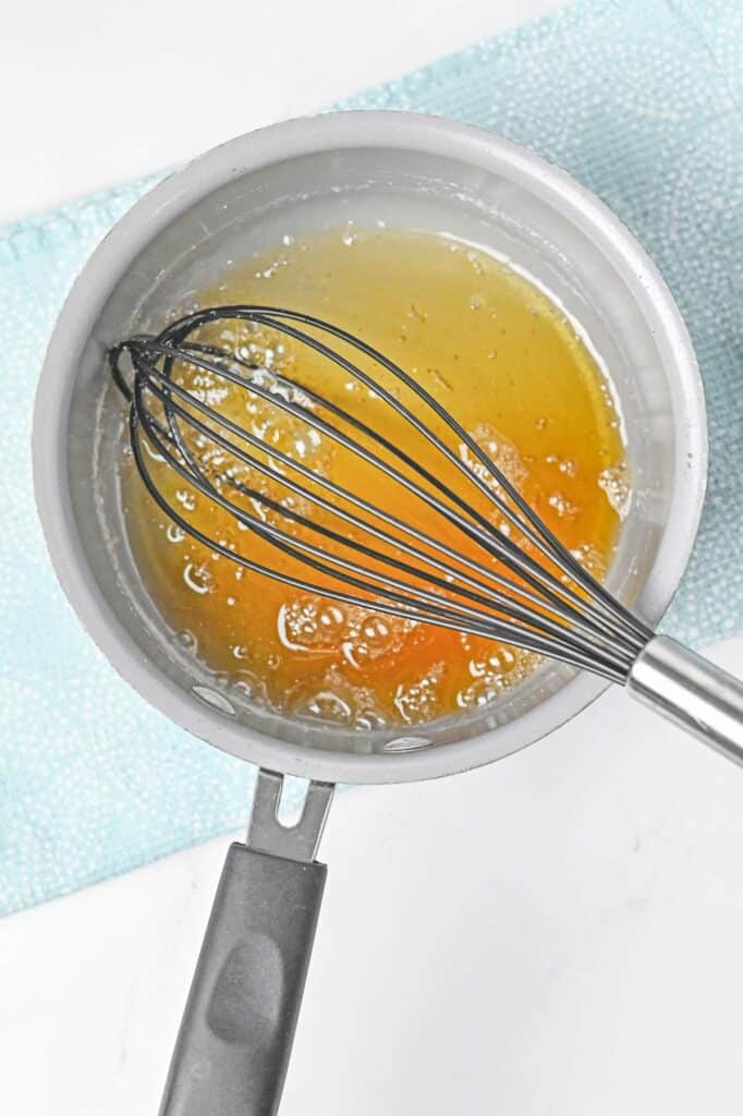 A saucepan with sugar mixture with a whisk in the middle of it.