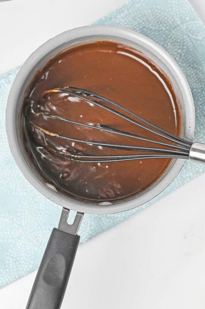 Chocolate ganache in a saucepan with a whisk.