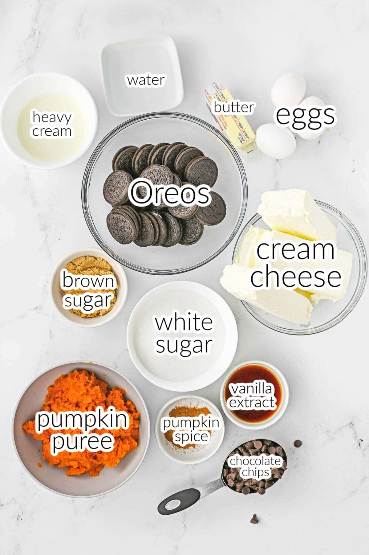 The ingredients for a chocolate pumpkin cheesecake - oreos, butter, eggs, chocolate chips, pumpkin puree, sugar, brown sugar, heavy cream, pumpkin pie spice, cream cheese, vanilla extract and water.