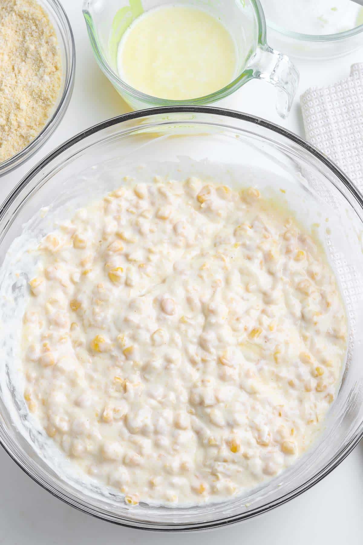 A bowl of corn casserole mixture in a glass mixing bowl.